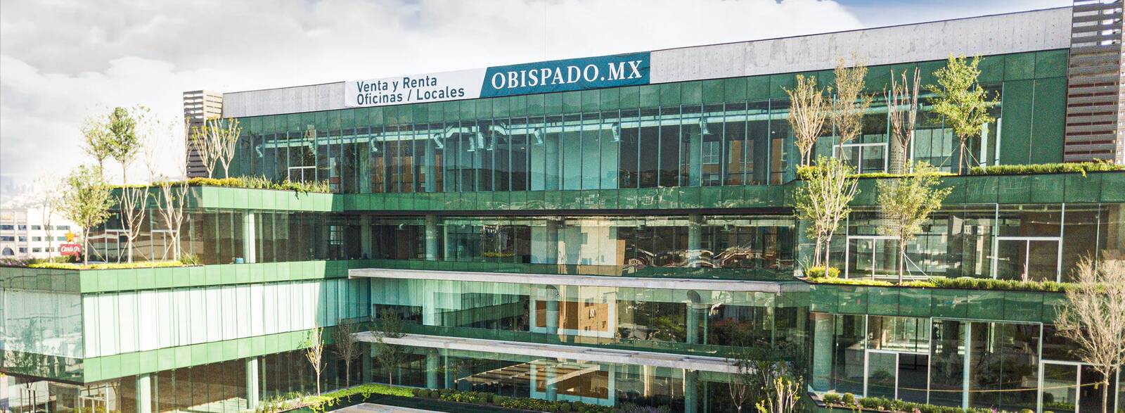Fachada de Paralelo Obispado: tres niveles de vidrio verde con jardineras y árboles en las terrazas